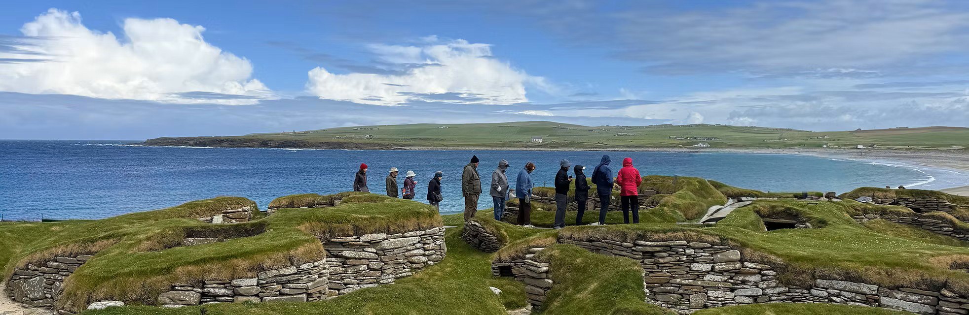 Travelers standing along the excavated Neolithic stone dwellings of Skara Brae above the sea in Orkney